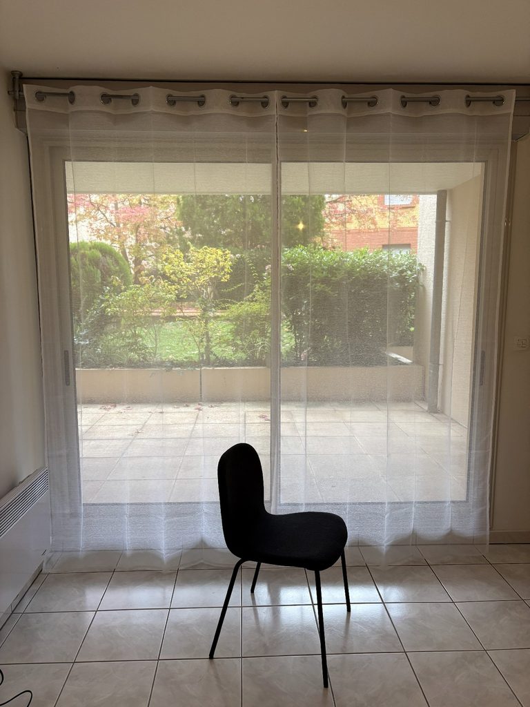 引っ越した日の、家具がない部屋。カーテンと椅子だけが置かれ、窓の外に庭が見える